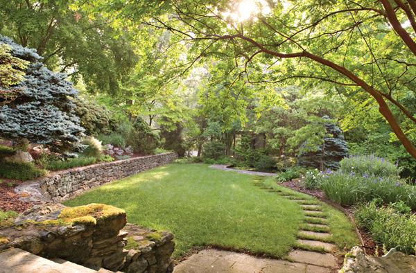In the sunken garden, gracefully curved drystack stone walls, a bluestone path with unusual 2” thick and 3’ x 4’ pavers, and a perennial border lead to a curved fish pond and bluestone surround. 