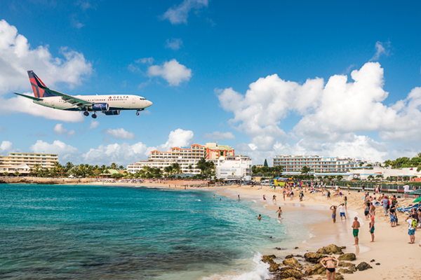 A jet approaches Princess Juliana Airport above onlookers on Maho Beach. The short runway gives beach goers close proximity views of the planes.